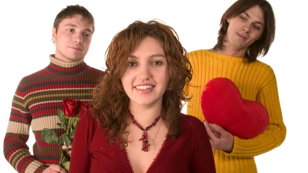 um homem segurando uma rosa vermelha, outro homem segurando um coração vermelho ambos tentando conquistar a mulher a sua frente.